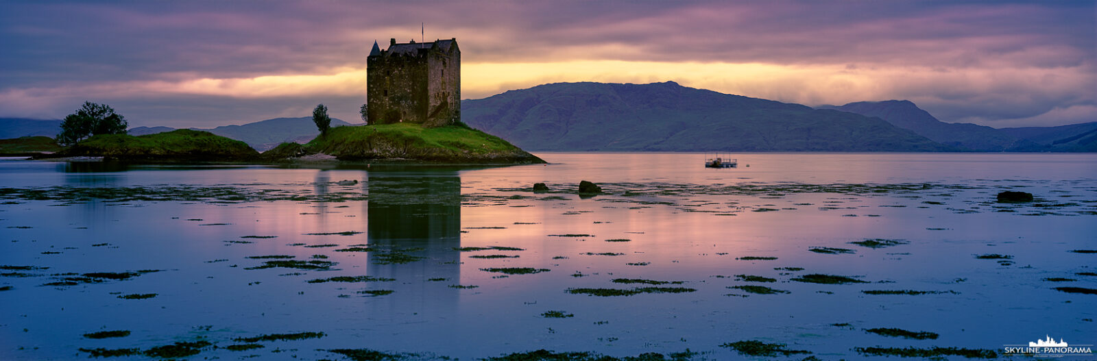 Panorama von Castle Stalker in der Dämmerung – Ein abendlicher Blick auf das historische Schloss, das majestätisch auf einer kleinen Insel im Loch Laich thront. Die sanften Farben des Sonnenuntergangs spiegeln sich im ruhigen Wasser und schaffen eine magische Atmosphäre. Castle Stalker, ein Wahrzeichen schottischer Architektur aus dem 15. Jahrhundert, ist umgeben von einer atemberaubenden Landschaft, die die Schönheit Schottlands perfekt einfängt.